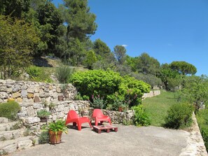 A patio area with stone walls, potted plants, and red plastic chairs.