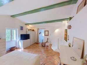 A bedroom with a bed, a TV, a desk, and a chair. There is a window and a door leading to another room.