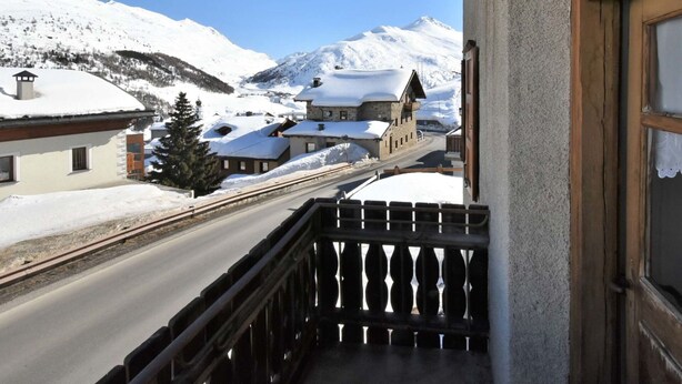 Un balcón con vistas a un pueblo cubierto de nieve en las montañas, que incluye una iglesia y edificios con tejados nevados.