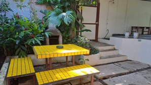 A yellow tiled outdoor table with a bench, surrounded by greenery and a concrete staircase.