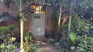A garden pathway leading to a door with a sign, surrounded by various tropical plants.