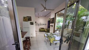 A dining area with a table set for four, a refrigerator, a sofa, and a ceiling fan.