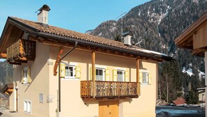 Een klassiek chalet met een houten balkon, schoorsteen en een berg als achtergrond.