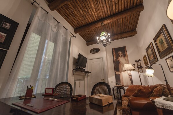 Un salon chaleureux avec un plafond en bois, un lustre, un canapé, un téléviseur et des tableaux encadrés accrochés aux murs.