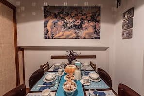 Une salle à manger avec une table dressée pour quatre personnes, agrémentée d’un centre de table, d’assiettes, de verres et d’un tableau accroché au mur.