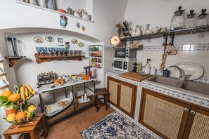 Een keuken met een houten tafel, een spoelbak en een aanrecht met diverse keukenbenodigdheden.