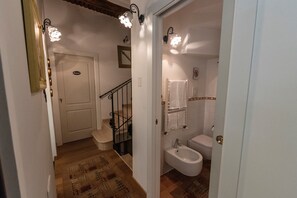 Un couloir menant à une salle de bain équipée de toilettes, d’un bidet et d’un petit tapis.