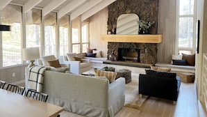 A spacious living room with a stone fireplace, large windows, and a high ceiling with exposed beams. - The Black Beaut Cabin (Black Butte Ranch)