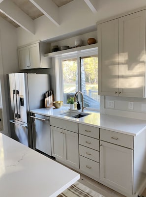 A modern kitchen with white cabinetry, a stainless steel refrigerator, and a window providing a view of the outdoors.