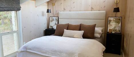Une chambre à coucher avec un grand lit, des murs en bois, deux tables de chevet avec des lampes et des œuvres d’art accrochées aux murs.