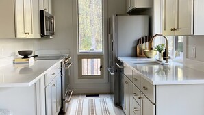 A modern kitchen with white cabinetry, stainless steel appliances, and a striped rug. - The Black Beaut Cabin (Black Butte Ranch)