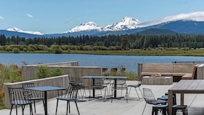 An outdoor seating area with tables and chairs overlooking a lake and mountains. - The Black Beaut Cabin (Black Butte Ranch)