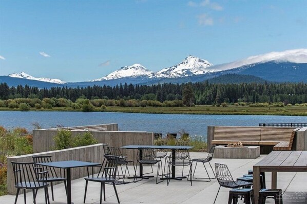An outdoor seating area with tables and chairs overlooking a lake and mountains.