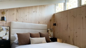 A bedroom with a wooden headboard, a large bed with white bedding, two nightstands with lamps, and artwork on the walls. - The Black Beaut Cabin (Black Butte Ranch)