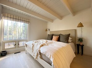 A bedroom with a large window, a bed with striped bedding, a headboard, and a bedside lamp.