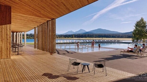 A wooden deck with a pool area, lounge chairs, and a view of mountains and a lake. - The Black Beaut Cabin (Black Butte Ranch)