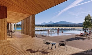 A wooden deck with a pool area, lounge chairs, and a view of mountains and a lake.