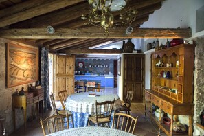 A rustic kitchen with wooden cabinets, a dining table, and chairs. There is a kitchen island with a sink and a stove. The kitchen has a stone backsplash and a chandelier.