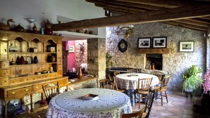 A rustic dining area with wooden furniture, stone walls, and a stone fireplace.