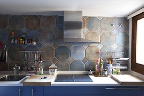 A modern kitchen with hexagonal stone backsplash, stainless steel appliances, and blue cabinets.