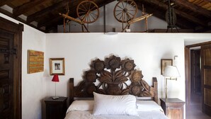 A bedroom with a wooden headboard, two wooden wheels, a red lamp, and a white bed.