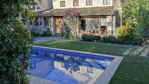 A pool with a tiled deck, surrounded by a well-maintained lawn and flowering plants.
