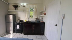 Une cuisine de taille réduite, équipée d’un réfrigérateur, d’une cuisinière et de meubles de rangement en bois foncé.