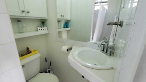 Une salle de bain comprenant des toilettes, un lavabo et un miroir. Des étagères se trouvent au-dessus des toilettes, où sont rangés les articles de toilette.