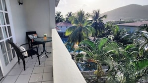 Un balcon avec une table et des chaises, donnant sur une piscine et des palmiers.