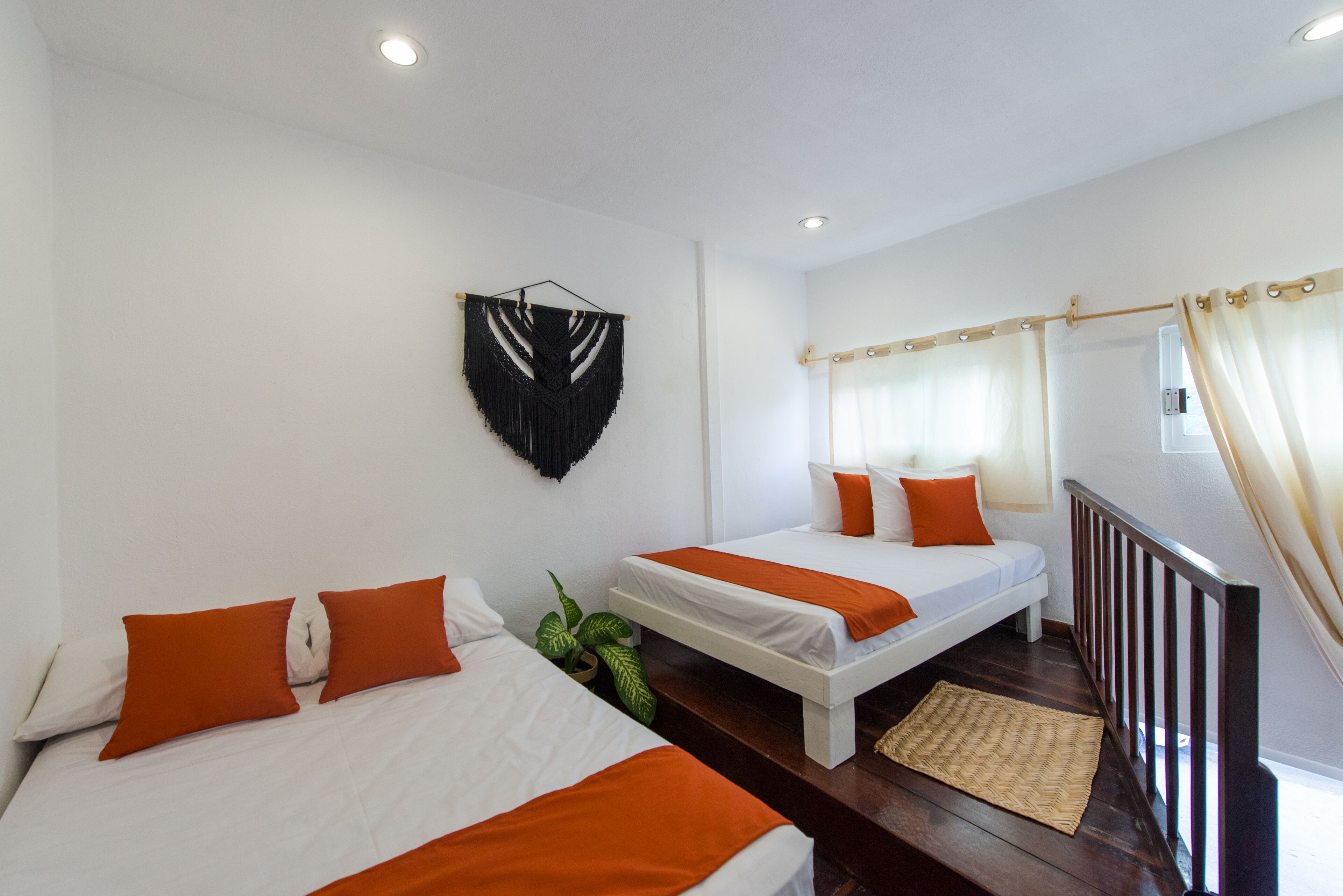 A hotel room with two beds, white bedding, orange pillows, a black wall hanging, and a wooden floor.