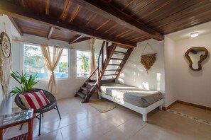 A bedroom with a wooden staircase, a bed, a chair, and a window with curtains. - Hotel Caracol Puerto Morelos (Puerto Morelos)