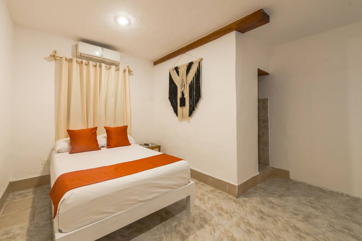 A bedroom with a bed, curtains, a wall-mounted air conditioner, and a decorative wall piece.