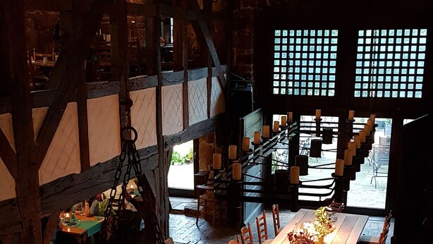 Una larga mesa de comedor con velas y flores, en una habitación rústica con vigas de madera a la vista y paredes de ladrillo.