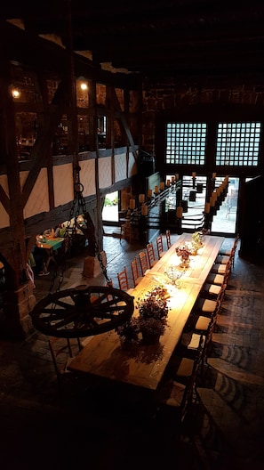 A long dining table with candles and flowers, set in a rustic room with exposed wooden beams and brick walls. - IN the Wetterburg - Holidays in the Middle Ages - knight time (Wetterburg)