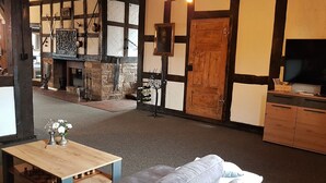 Una habitación tradicional con vigas de madera a la vista, una chimenea de piedra, una mesa de madera con piezas de ajedrez y un sofá gris.