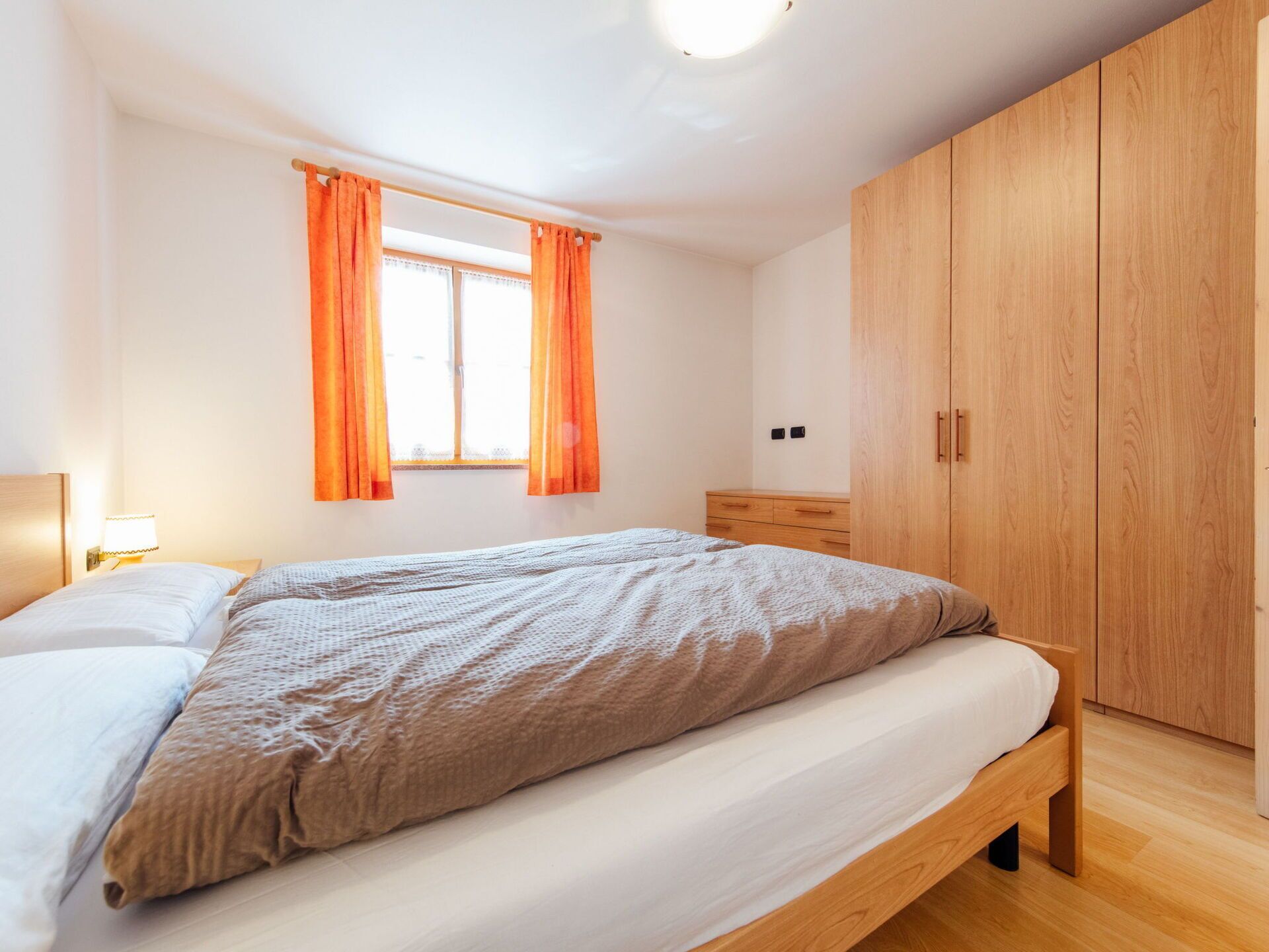 A bedroom with a bed, a nightstand, a wardrobe, and a window with curtains.