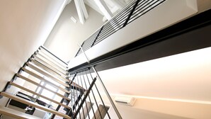 Una escalera moderna con barandilla de metal y vistas a una habitación con cama y mesita de noche.