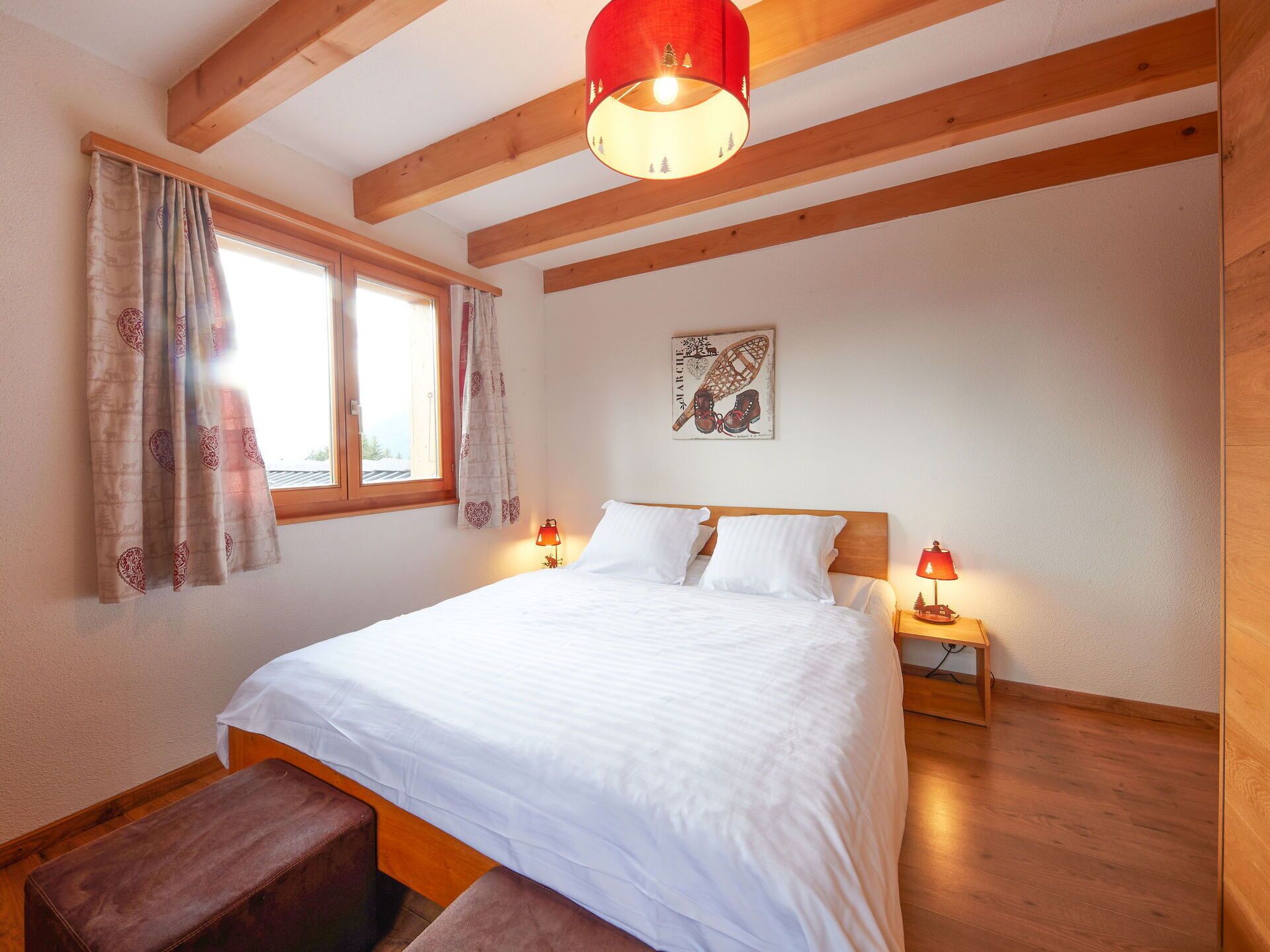 A bedroom with a wooden ceiling, a bed with white bedding, two bedside lamps, a window with curtains, and a wall-mounted artwork.