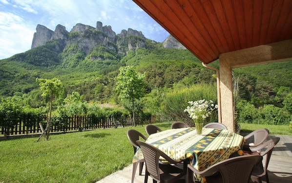 An outdoor patio with a table and chairs, a wooden fence, and a mountain backdrop.