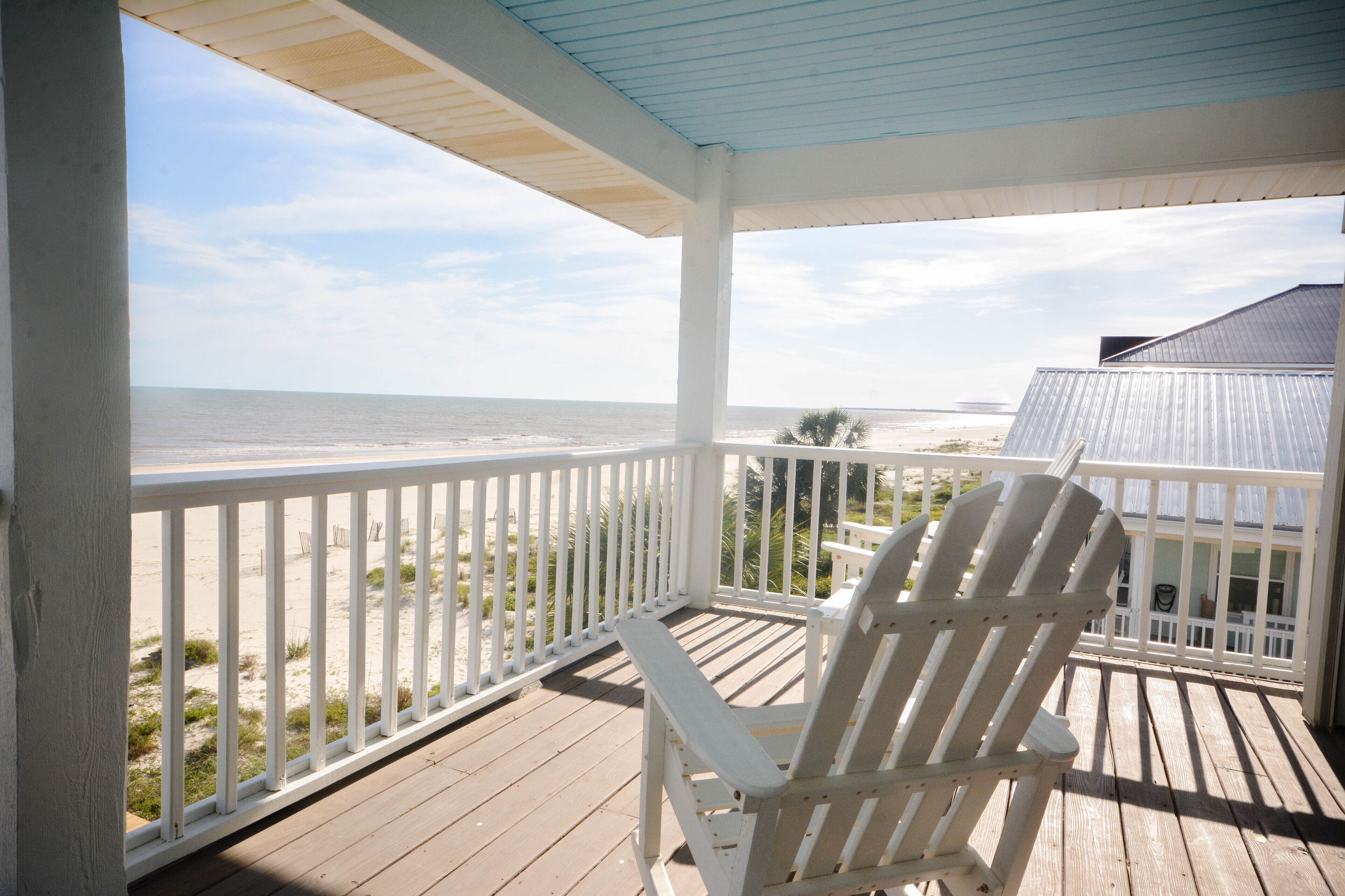 Une terrasse en bois avec une chaise blanche donnant sur la plage.