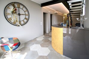 A modern interior with a large wall clock, a unique seating area, and a staircase.