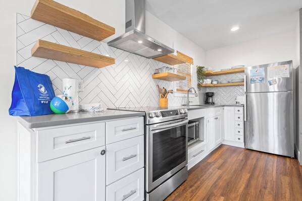 A modern kitchen with white cabinetry, a stainless steel oven, a built-in microwave, wooden shelves, and a stainless steel refrigerator.