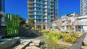Un bâtiment moderne, avec un ciel bleu dégagé, une petite fontaine et un chemin pavé de pierres.