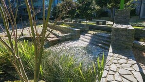 Une fontaine en pierre avec une petite cascade, entourée de verdure et de sentiers en pierre.