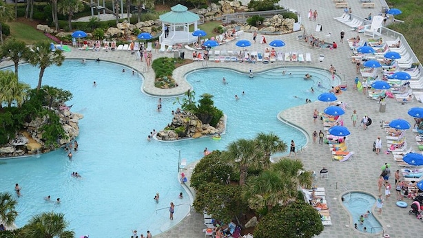 A large outdoor swimming pool area with multiple pools, lounge chairs, umbrellas, and a gazebo. - Premier Partner Oceanfront Edgewater Condo With Full Amenities (Panama City)
