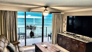 A living room with a large TV, a sofa, a coffee table, and a balcony with a view of the ocean. - Premier Partner Oceanfront Edgewater Condo With Full Amenities (Panama City)