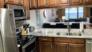A kitchen with wooden cabinets, stainless steel appliances, a granite countertop, and a view of the ocean. - Premier Partner Oceanfront Edgewater Condo With Full Amenities (Panama City)