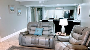 A living room with a gray leather sofa, a blue pillow, and a wooden coffee table. - Premier Partner Oceanfront Edgewater Condo With Full Amenities (Panama City)