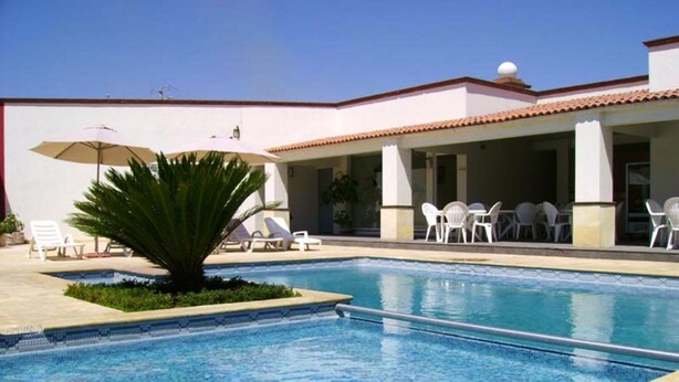 A swimming pool with lounge chairs and umbrellas, surrounded by a building with a tiled roof. - Hotel San Juan Park (San Juan del Río)