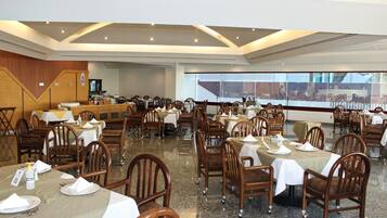 Un amplio comedor con varias mesas y sillas, una barra y un ventanal con vistas.